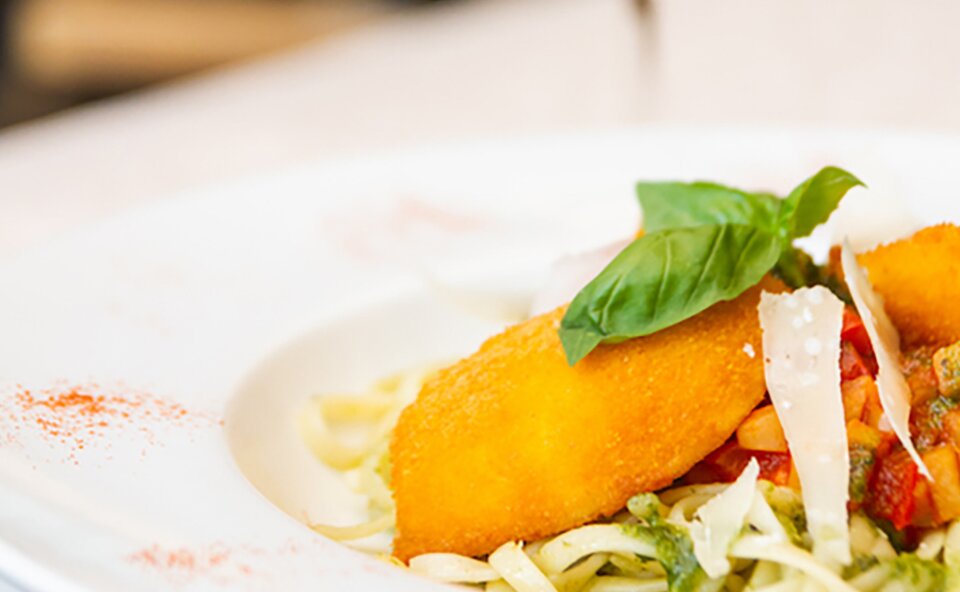 Paniertes Filet auf Pasta mit Pesto, Tomaten, Parmesan und Basilikum im weißen Teller. Paniertes Filet auf Pasta mit Pesto, Tomaten, Parmesan und Basilikum im weißen Teller.